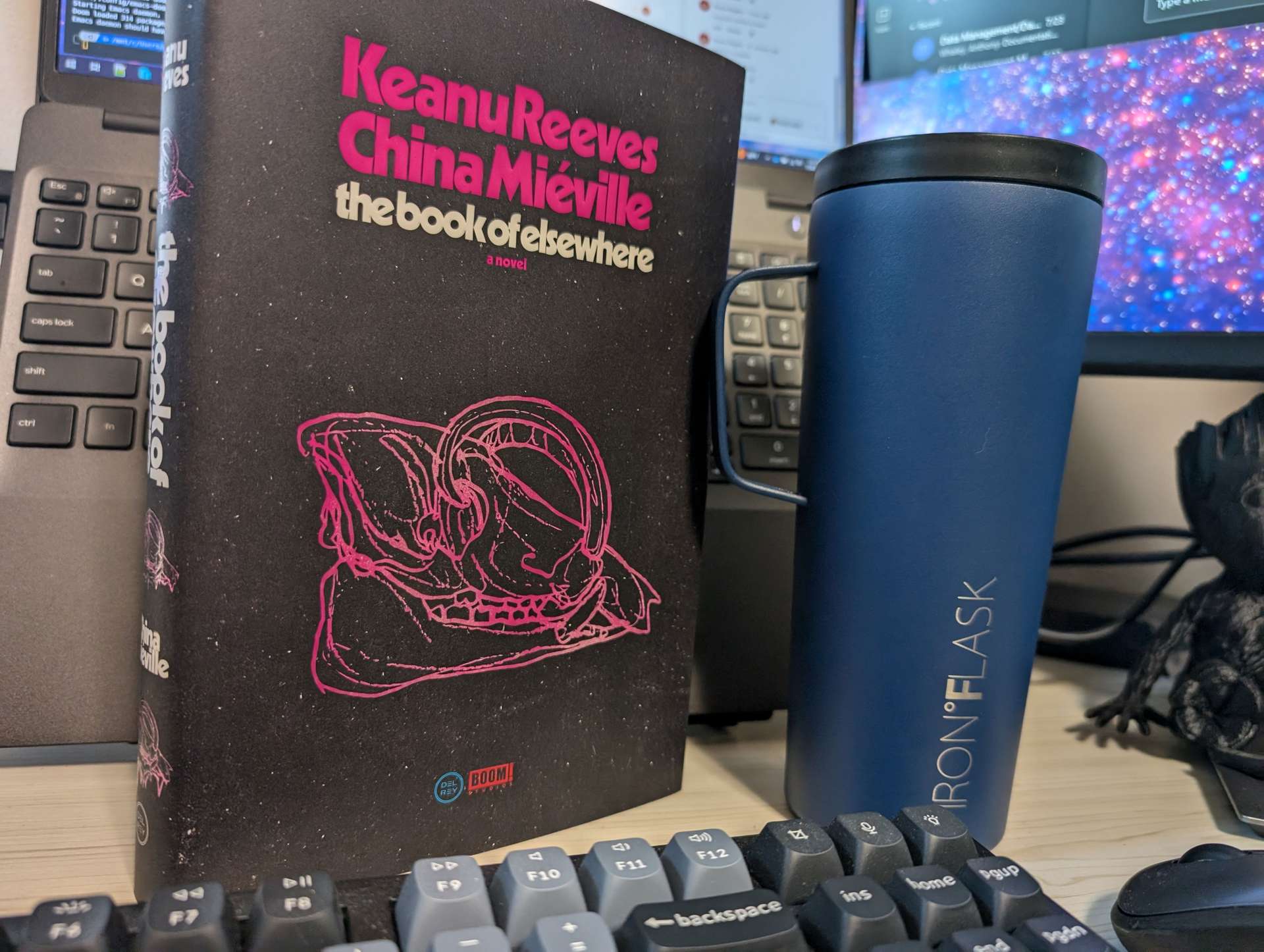 Photo of the book, "the book of elsewhere" by the authors Keanu Reeves and China Miéville. Next to the book is my blue coffee canister.